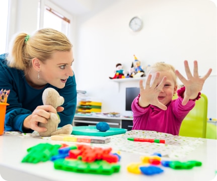 Toddler girl in child occupational therapy session doing sensory playful exercises with her therapist